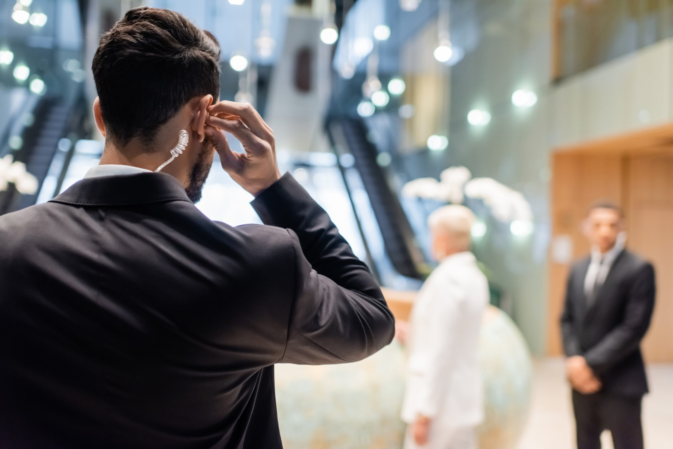 back view of bi-racial security man adjusting earpiece near blurred businesswoman and african american bodyguard,stock image