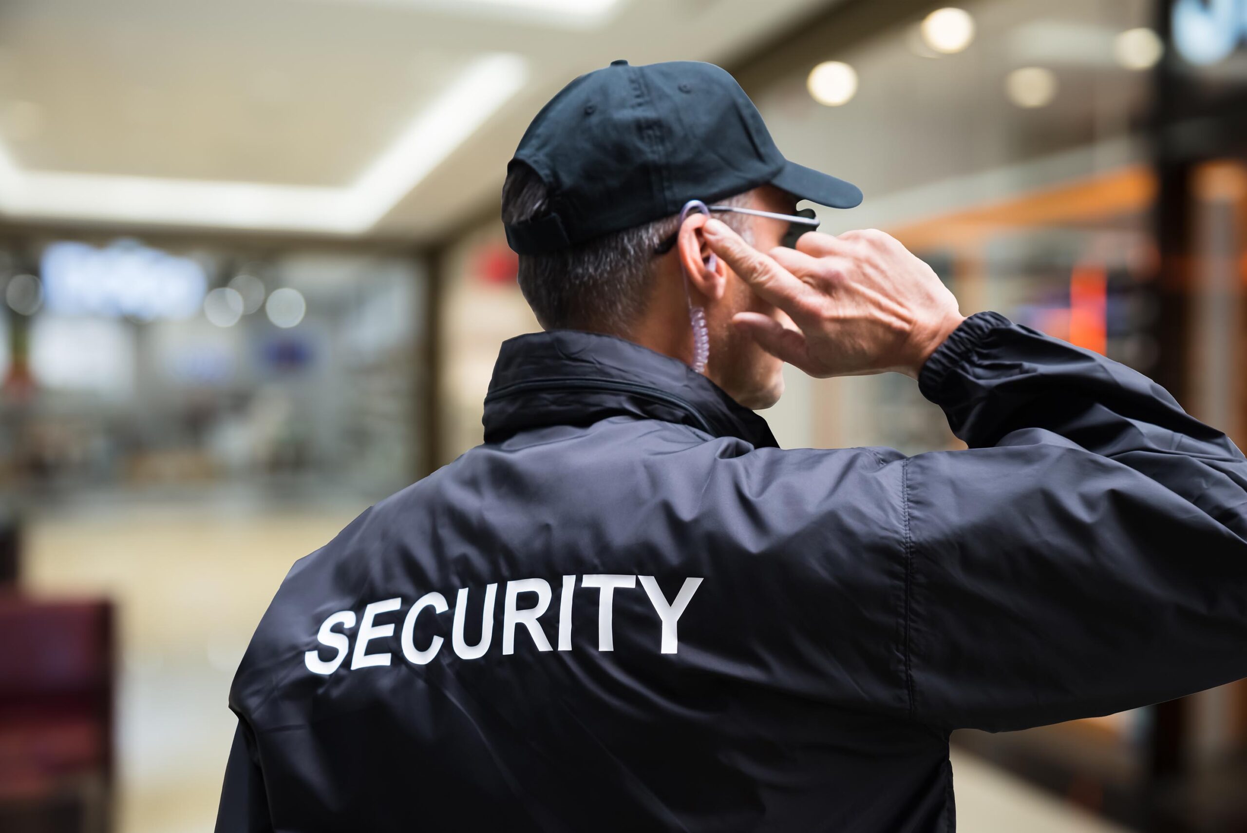 Rear view of mature security guard listening to earpiece against building