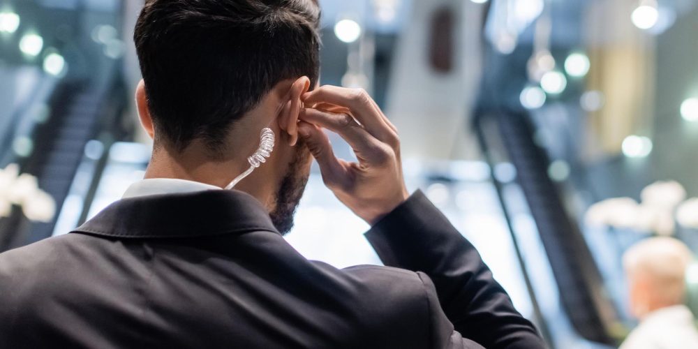 back view of bi-racial security man adjusting earpiece near blurred businesswoman and african american bodyguard,stock image