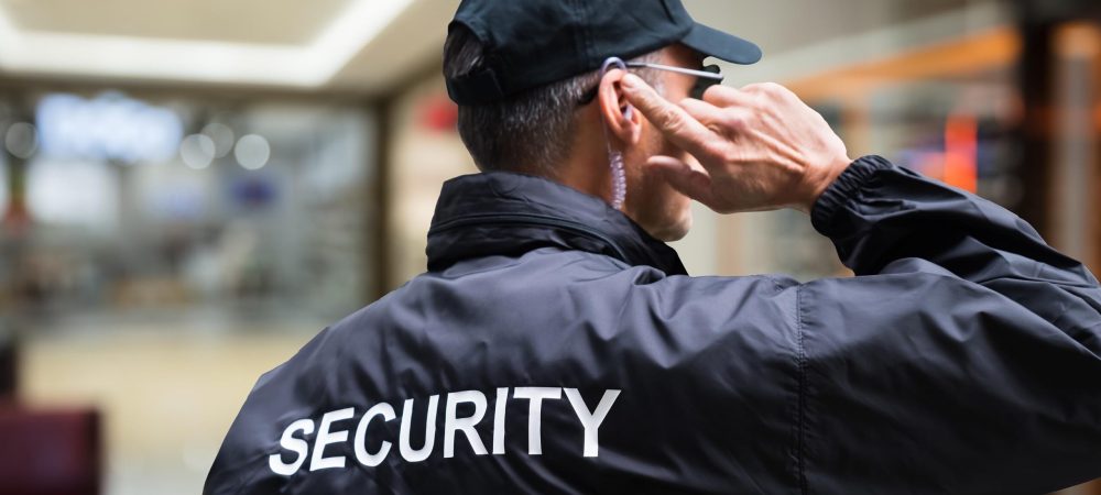 Rear view of mature security guard listening to earpiece against building