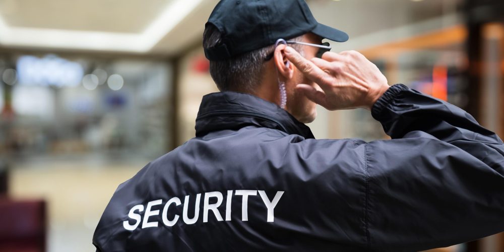 Rear view of mature security guard listening to earpiece against building